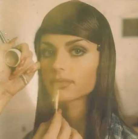 Vintage-style photo of a woman with long dark hair and green eyes as lip color is applied with a small brush