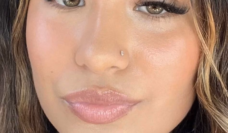 Close-up of a woman's face with soft pink glossy lips, a small nose stud and light brown wavy hair