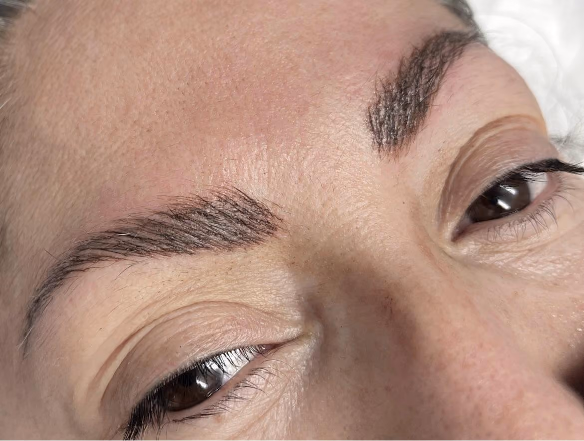 Close-up of a woman's tilted face showing two eyebrows with fine dark hair-like strokes