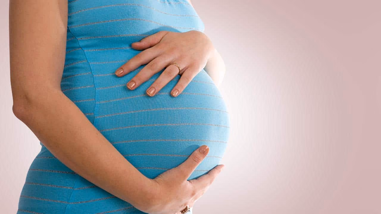 Pregnant woman in a blue striped top cradling her belly with both hands