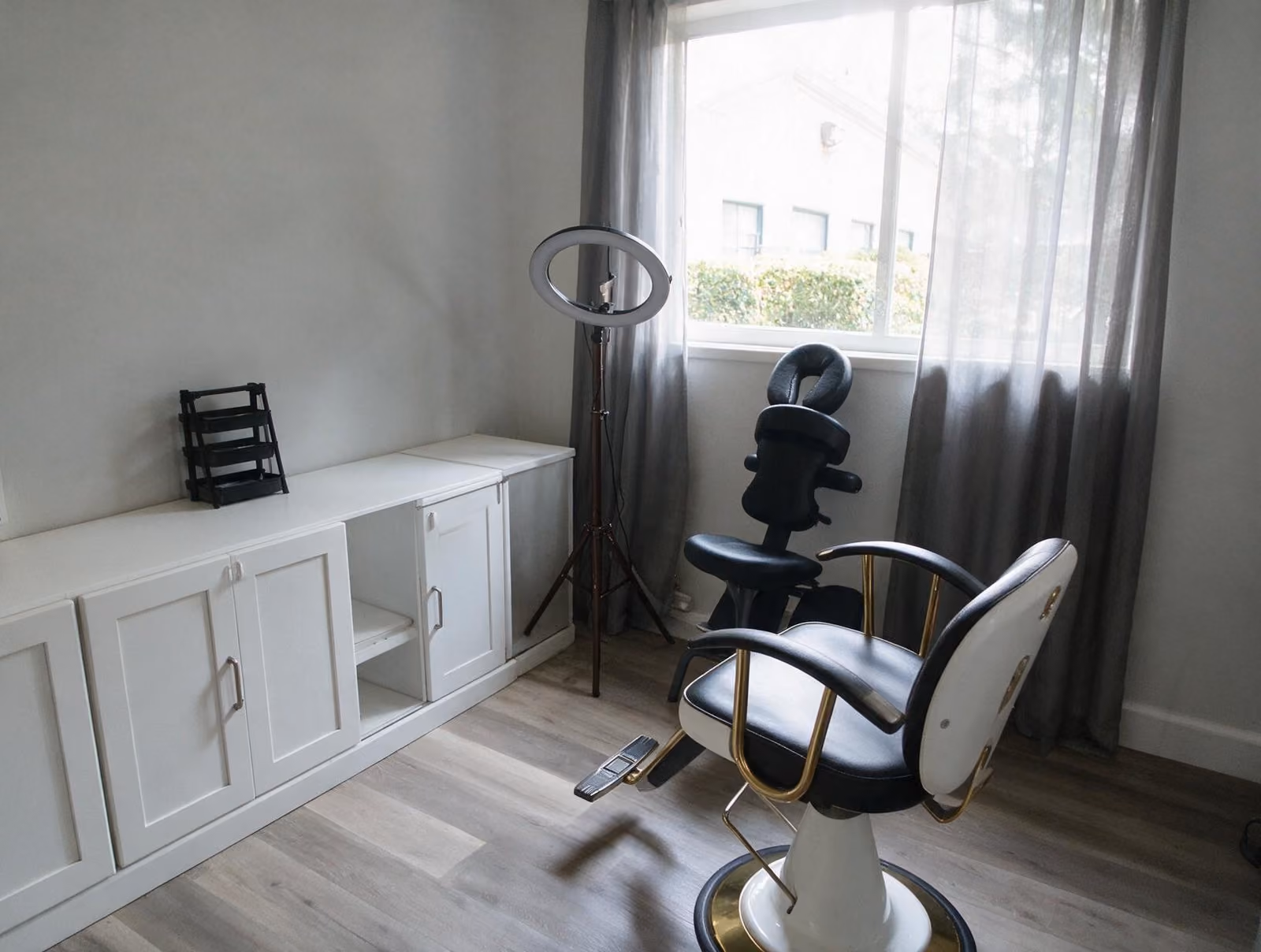 Quiet treatment room with a black and white reclining chair, a ring light on a tripod and a massage chair by the window